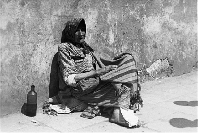 Jewish woman sits against a wall on the street in the Warsaw ghetto